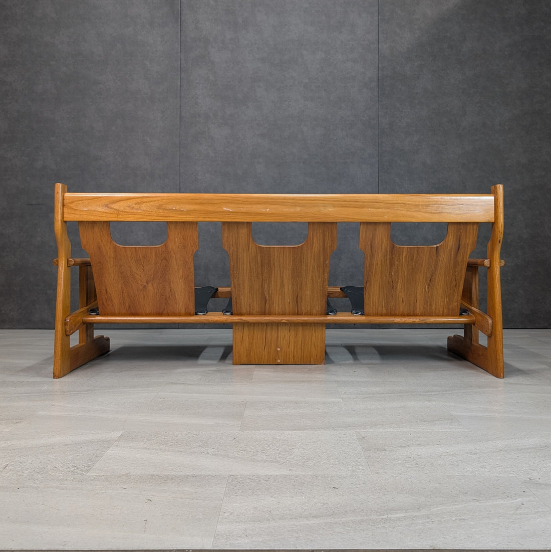 Straight rear view of 1970s Brutalist rosewood sofa showing three cutout back panels and timber base