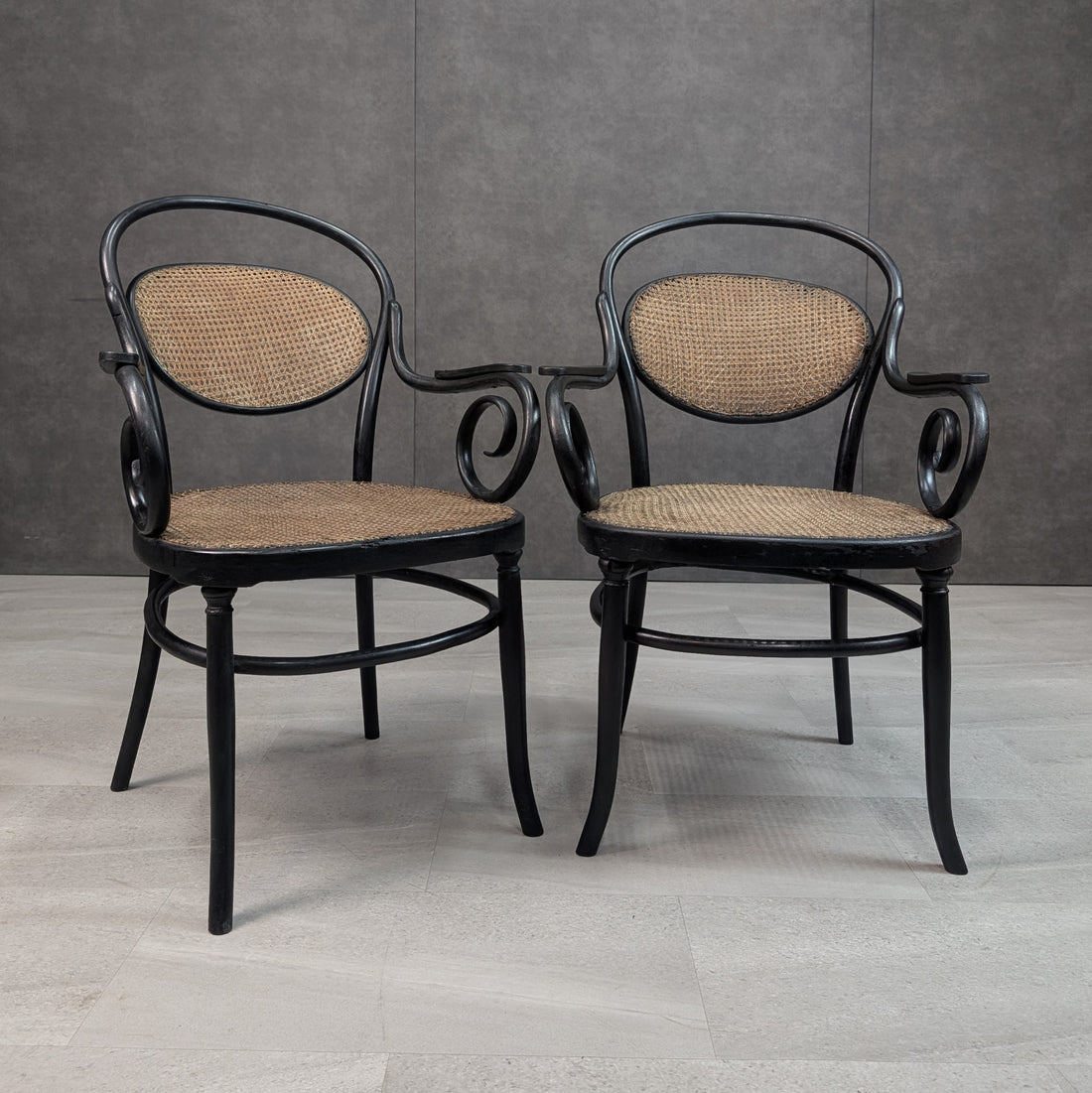 Two antique Thonet No 11 style black bentwood armchairs with cane backs and seats, front view