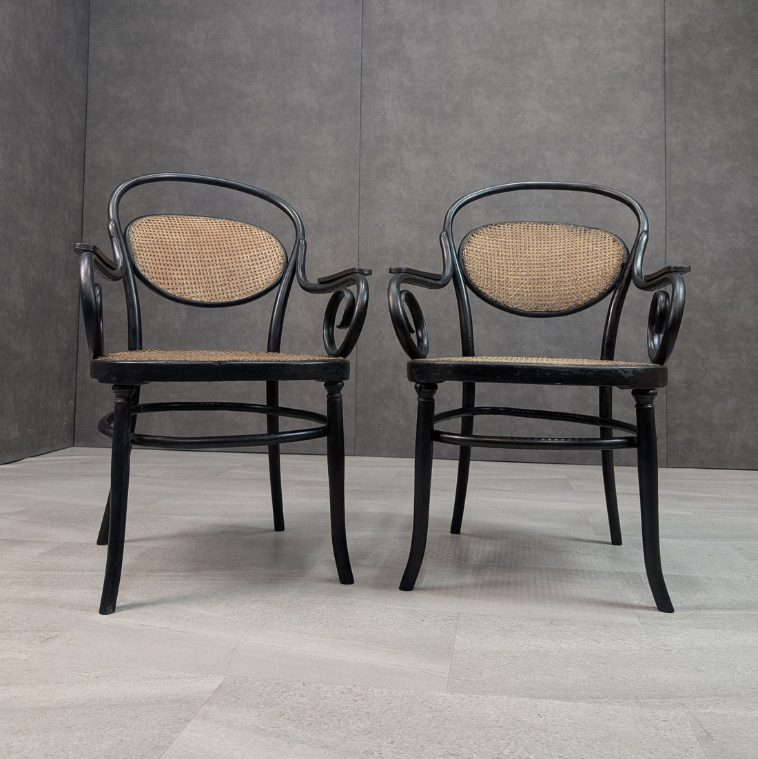 Front view of two black antique bentwood chairs with woven cane seating and circular stretchers