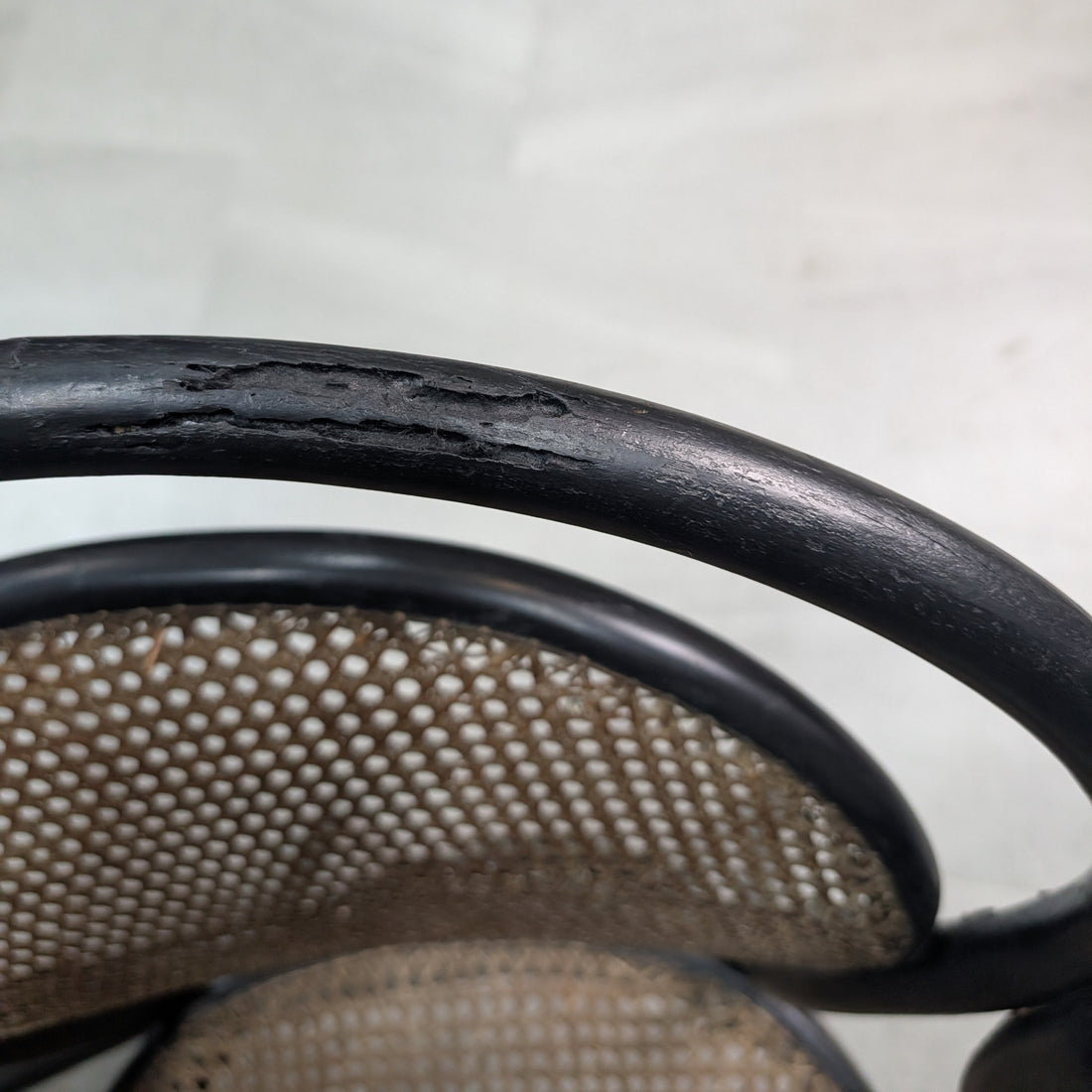Close up of evidence of woodworm and wear to black finished curved bentwood chair frame