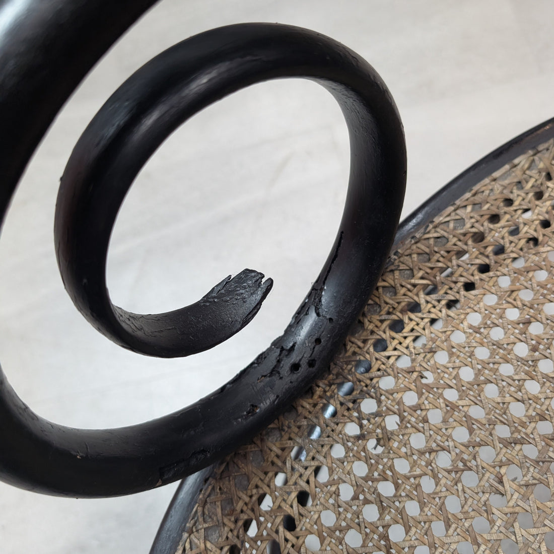 Close up of bentwood scroll arm showing surface wear and apparent woodworm evidence adjacent to cane seat