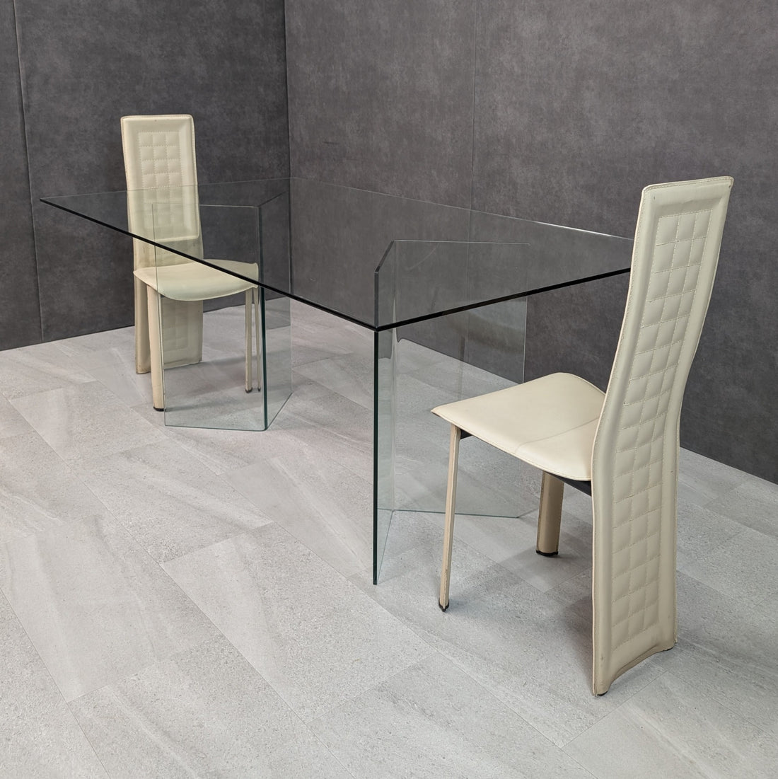 FIAM style clear glass dining table with folded transparent glass supports, angled view with two chairs for scale