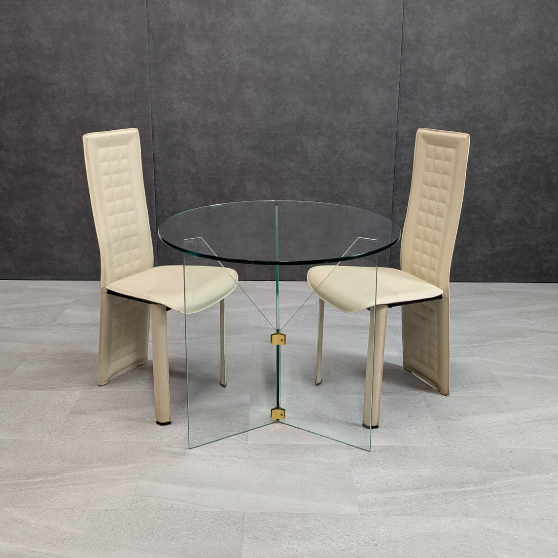 Original Harper Fredericks 80cm round clear glass dining table with vintage brass fittings shown between two cream dining chairs