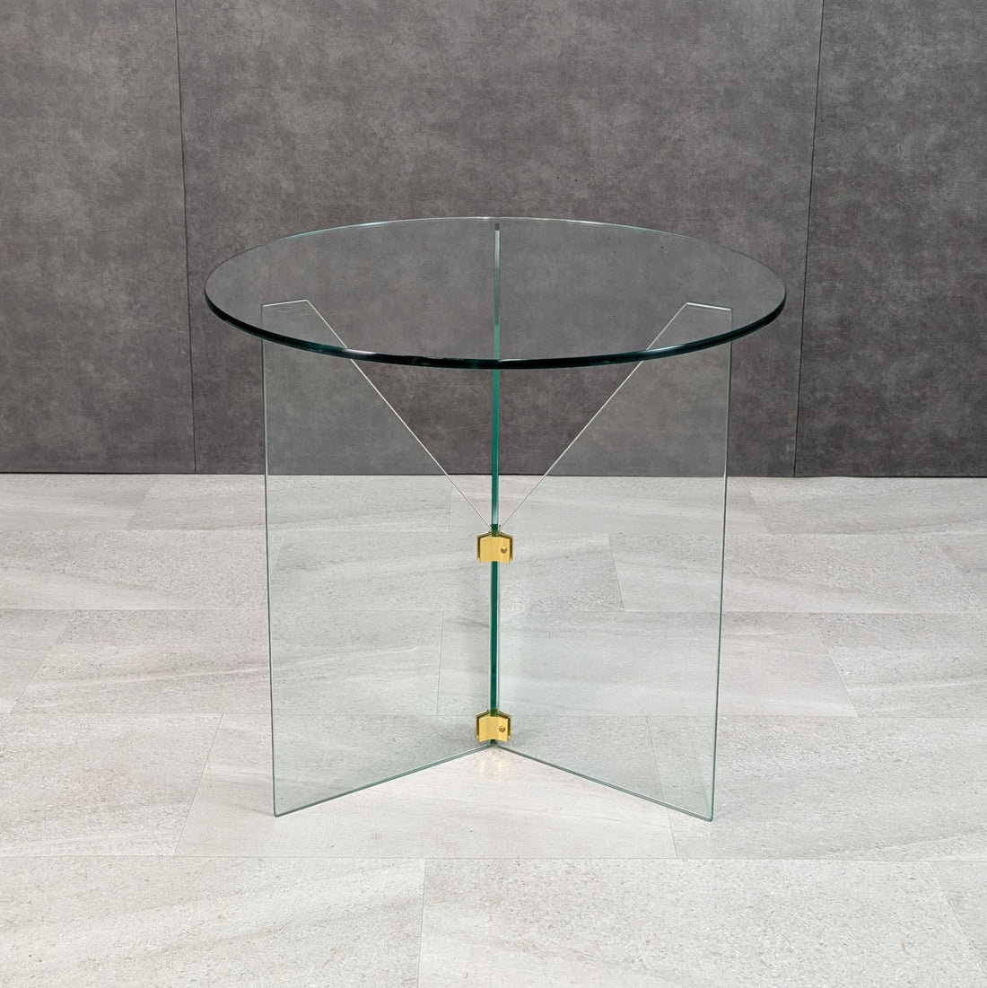 Contemporary round all glass table showing intersecting transparent glass planes and brass connection fittings