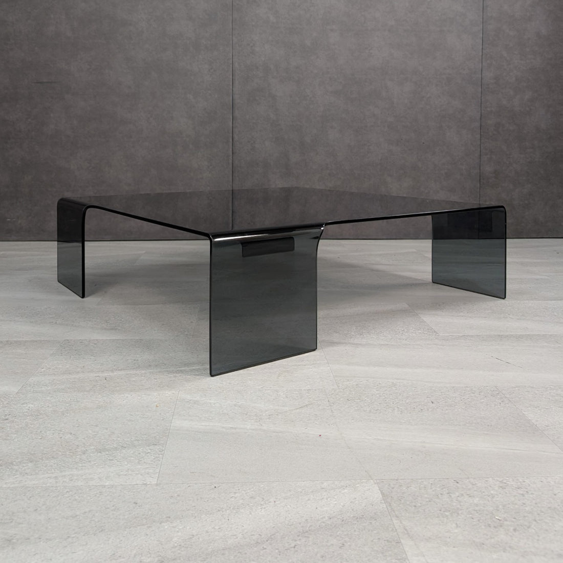 Smoked grey bent glass coffee table in the style of FIAM Neutra, three-quarter view showing four broad waterfall legs