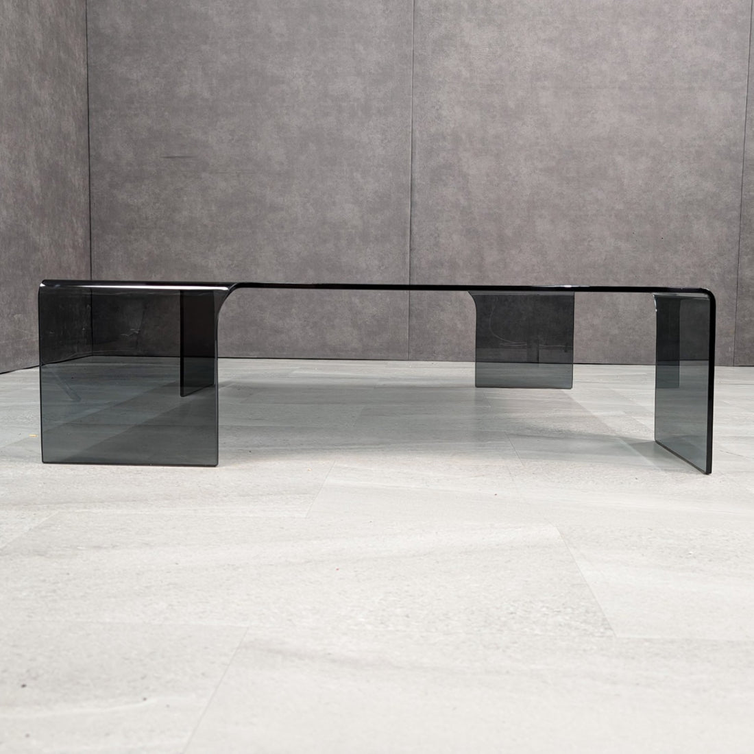 Low front view showing the broad square top and offset waterfall legs in smoked grey glass