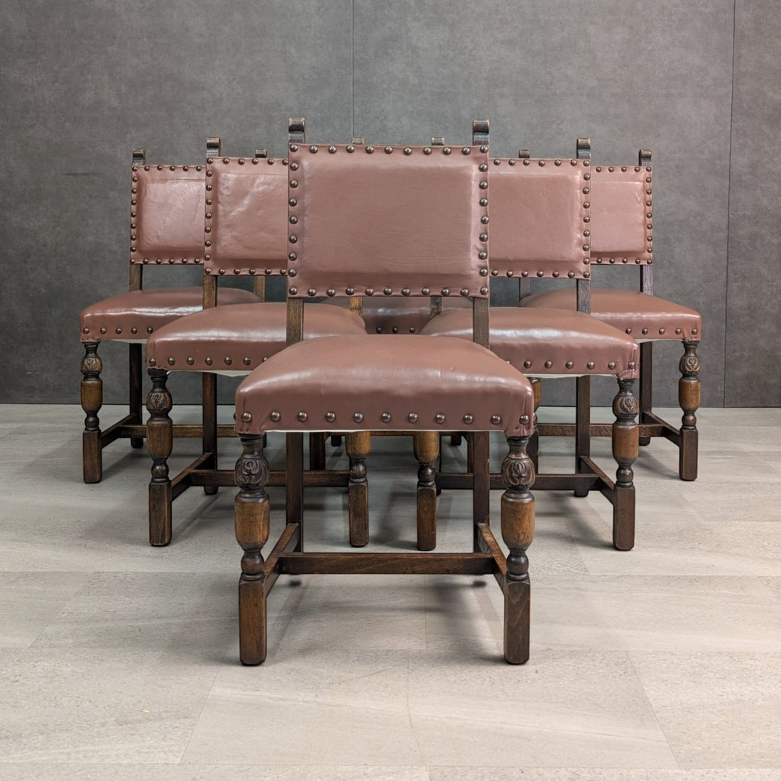 Front view of six English oak dining chairs showing studded leather backs and carved turned front legs