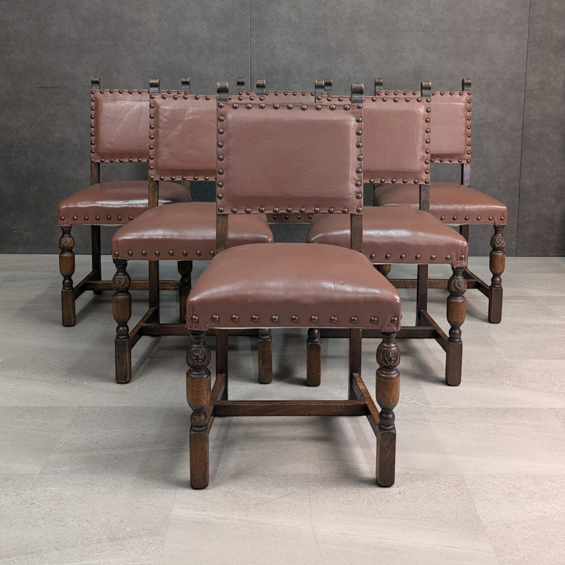 Group of six Jacobean Revival dining chairs showing brown leather seats, decorative studs and oak stretchers