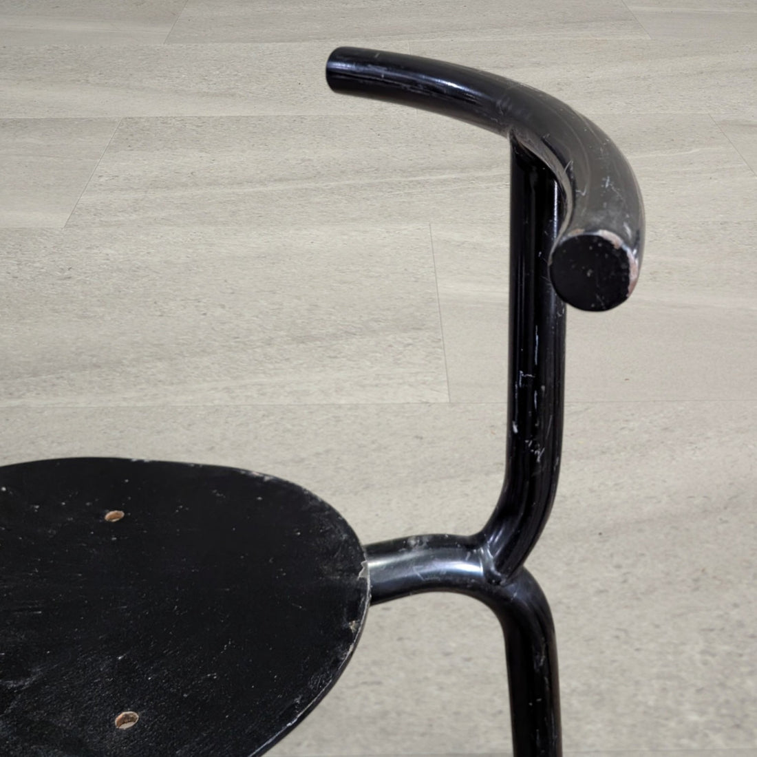 Close-up of curved tubular steel chair back showing worn black paint
