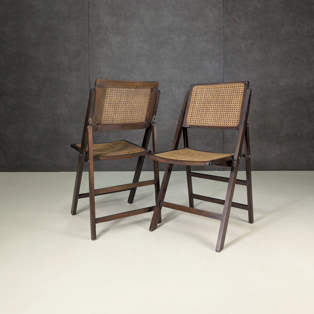 Two vintage mid-century dark timber and woven cane folding chairs, front view