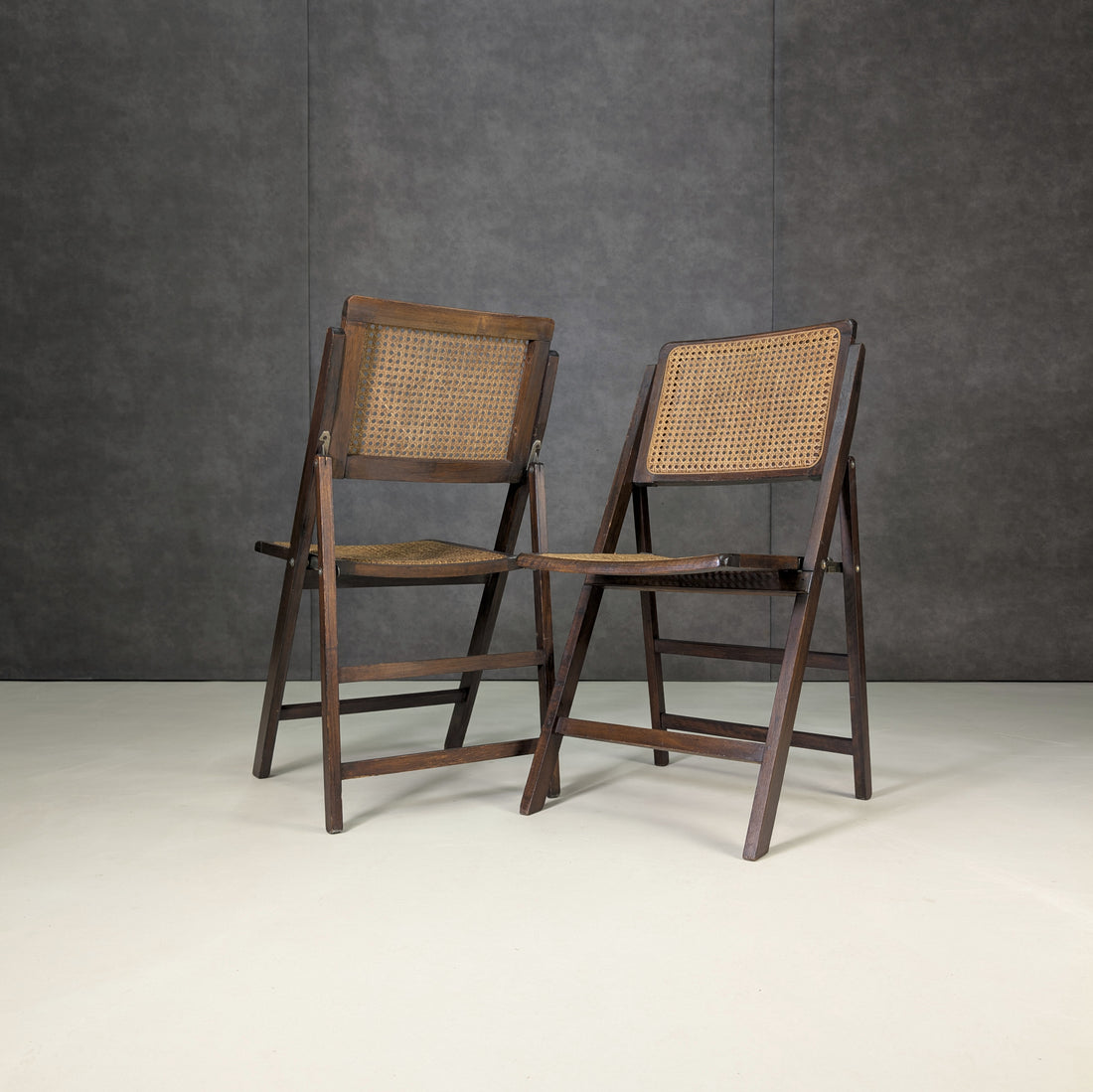 Pair of dark timber and cane folding chairs shown at an angle