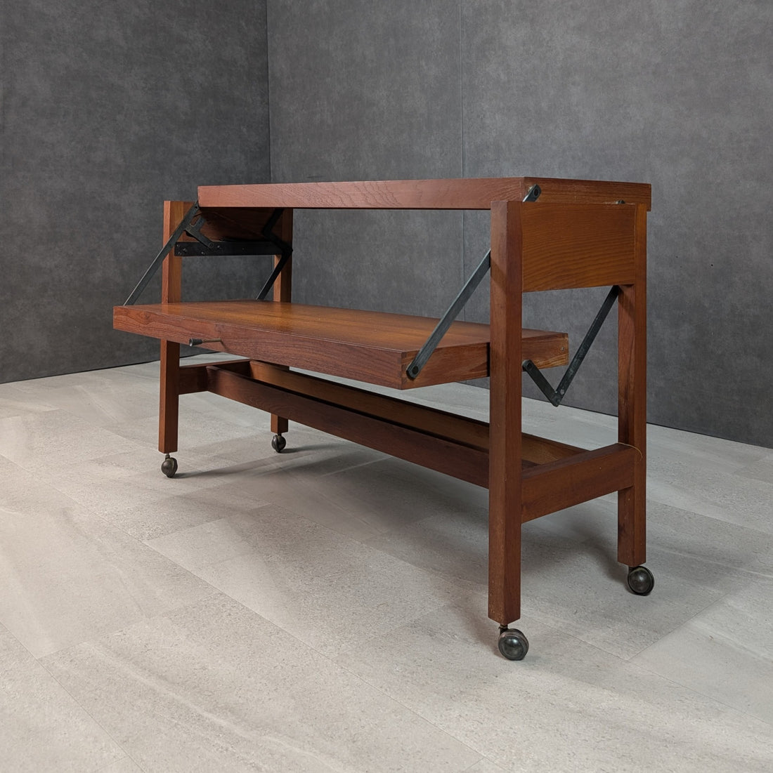 Articulating teak table showing exposed black metal pivot arms and lifting wooden surfaces