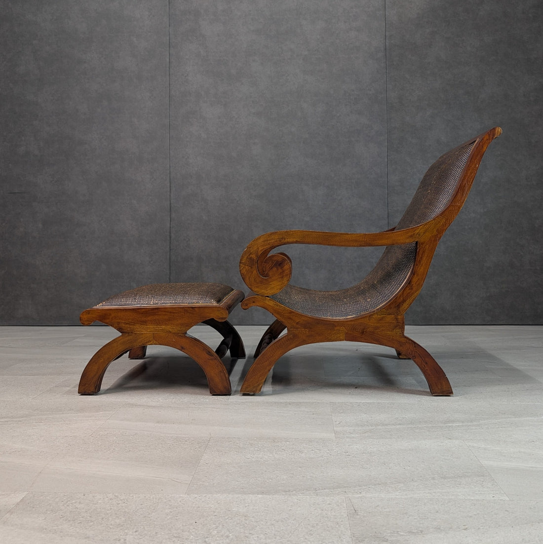 Side profile of plantation lounge chair and matching ottoman showing reclined back, carved scroll arms and arching timber legs