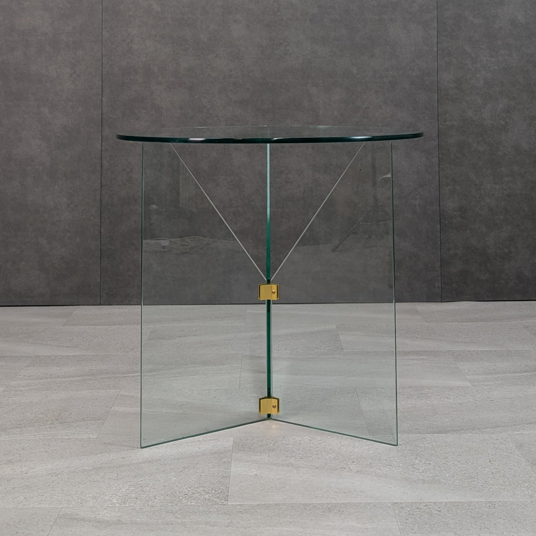 Front view of 80cm round clear glass dining table with transparent triangular glass base and brass hardware
