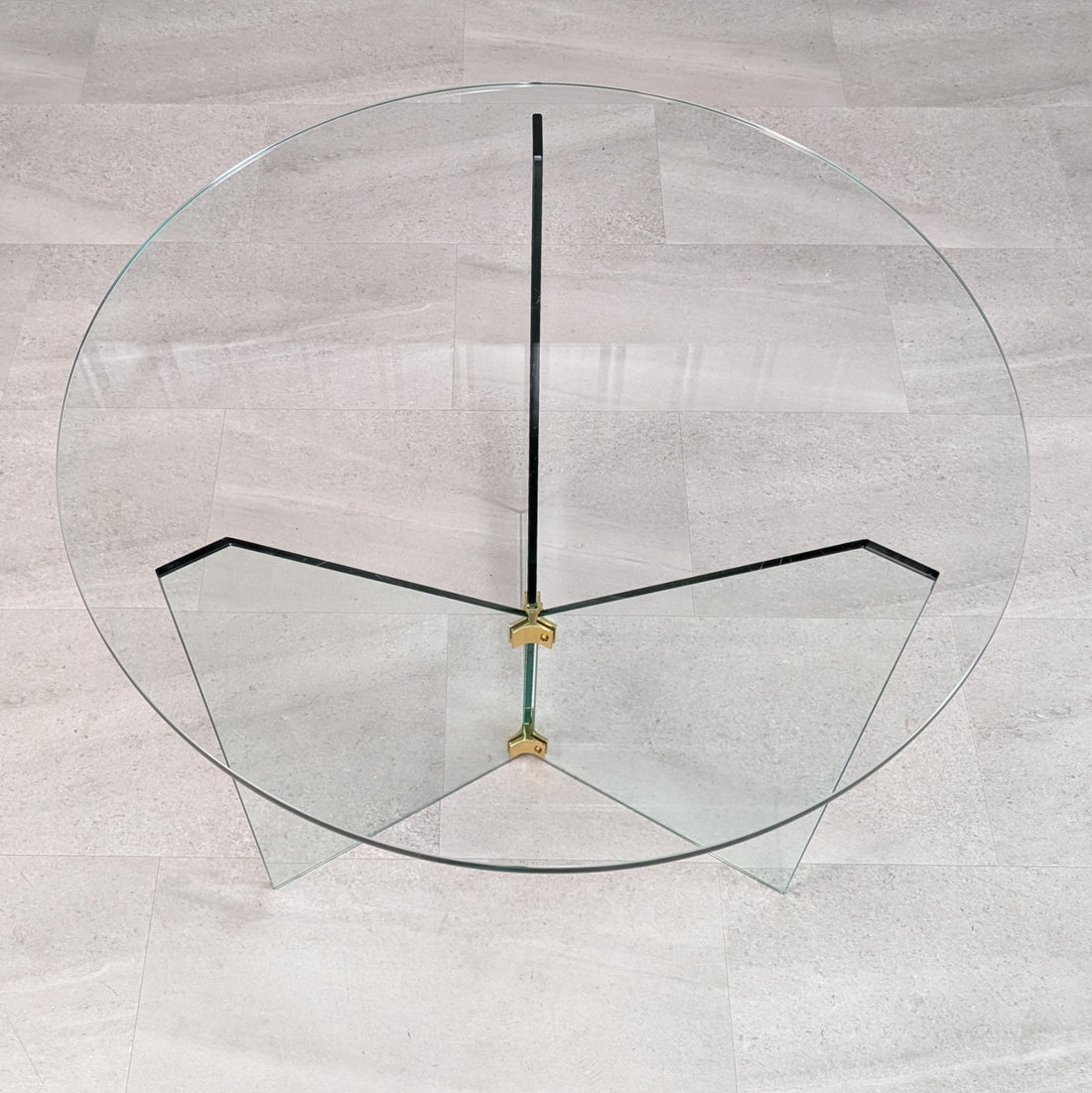 Overhead view of compact round glass dining table with three radiating glass support panels and brass joints
