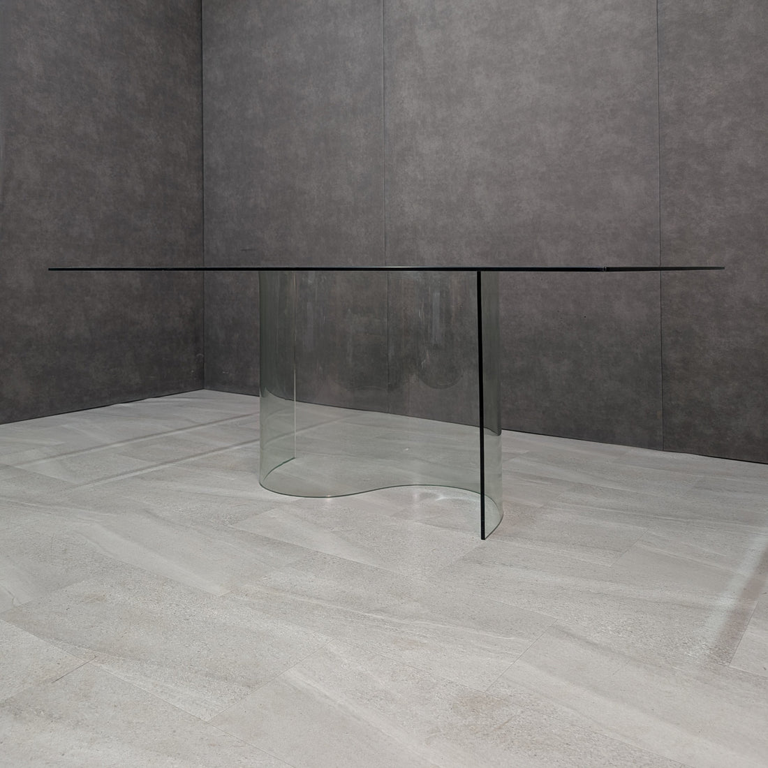 Clear glass dining table with S shaped pedestal and bevelled top, angled view