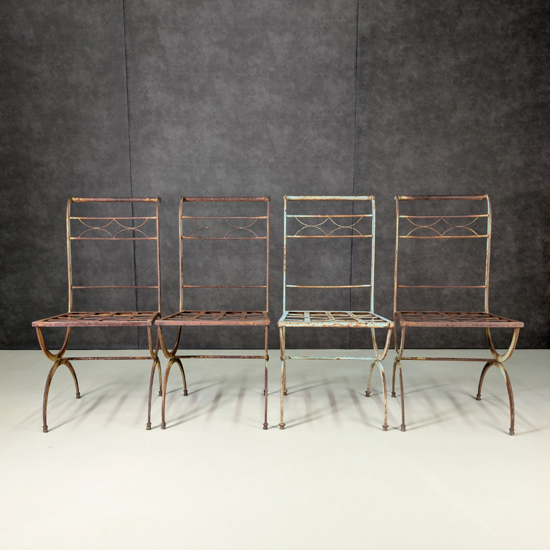 Four matching wrought iron garden chairs with aged powder blue paint and oxidation, front view