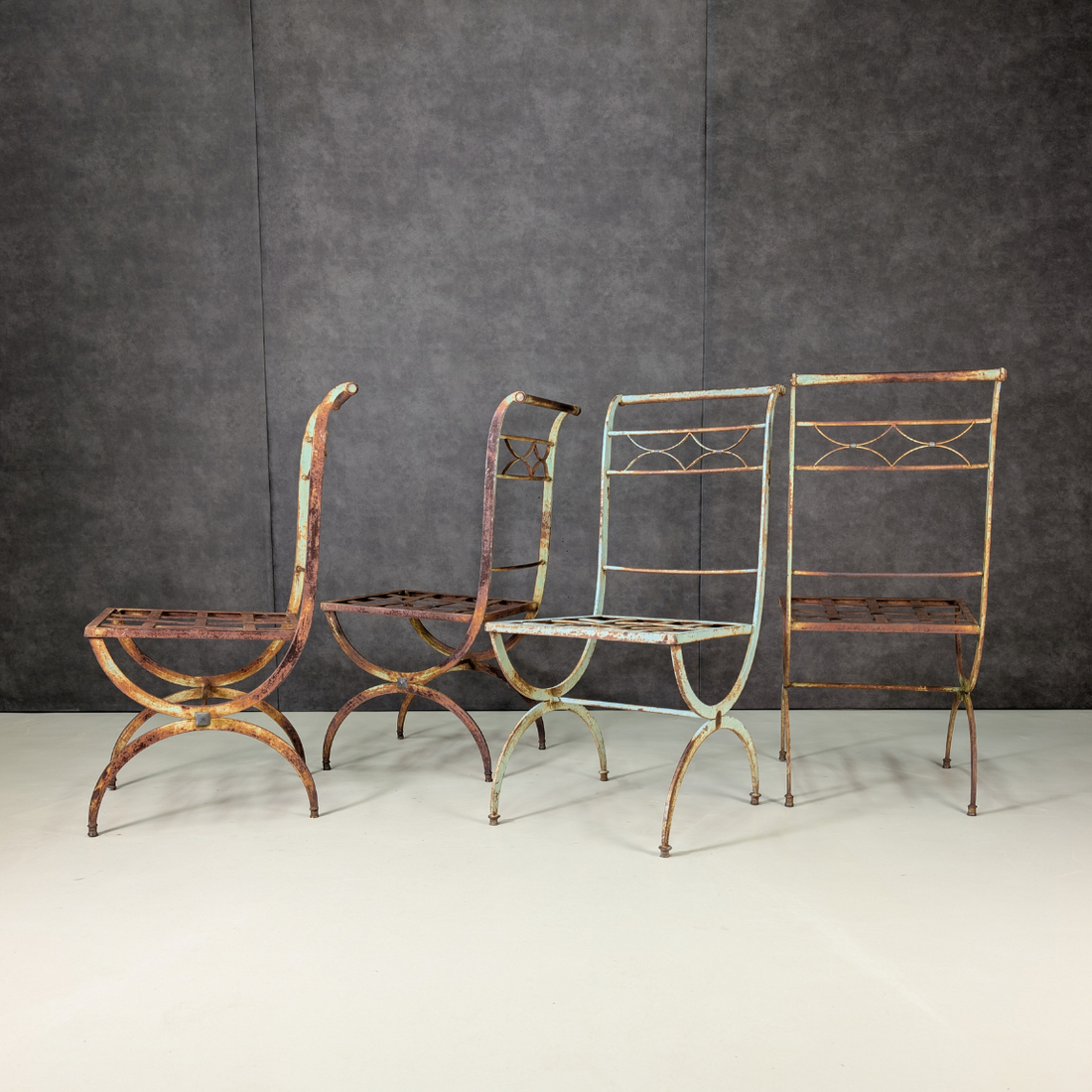 Four wrought iron garden chairs showing curved legs and side profiles